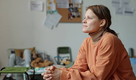 Kvinna på trygghetspunkt med knutna händer, barn liggande i soffa och anslagstavla med foton på