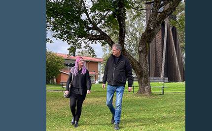 Två av våra upphandlare, Sara och Hans, promenerar vid klocktornet i Charlottenberg, blå bakgrund