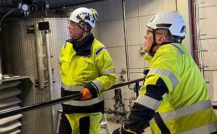 Två män i varselkläder och hjälm på en energianläggning